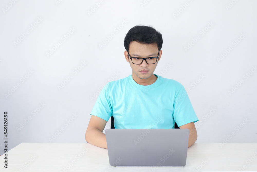 Young Asian Man is serious and focus when working on a laptop and document on the table. Indonesian man wearing blue shirt.