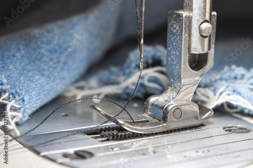 Needle presser foot with thread of white industrial sewing machine with blue jeans close-up.