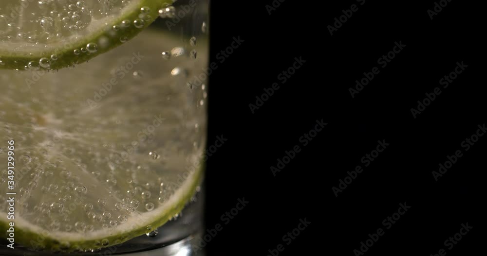 macro sparkling water with lemon and lime with bubbles and ice on a black background. Lemonade in glass macro sparkling water with lemon and lime with bubbles and ice on a black background. Lemonade in glass