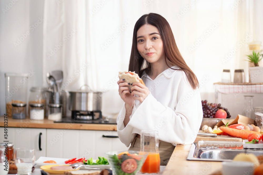 Young Asian woman in the kitchen eating sandwich for breakfast, Healthy food concept