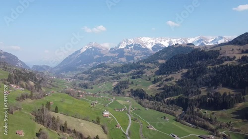 Drone flight through a green swiss valley in the alps with snow and blue sky photo