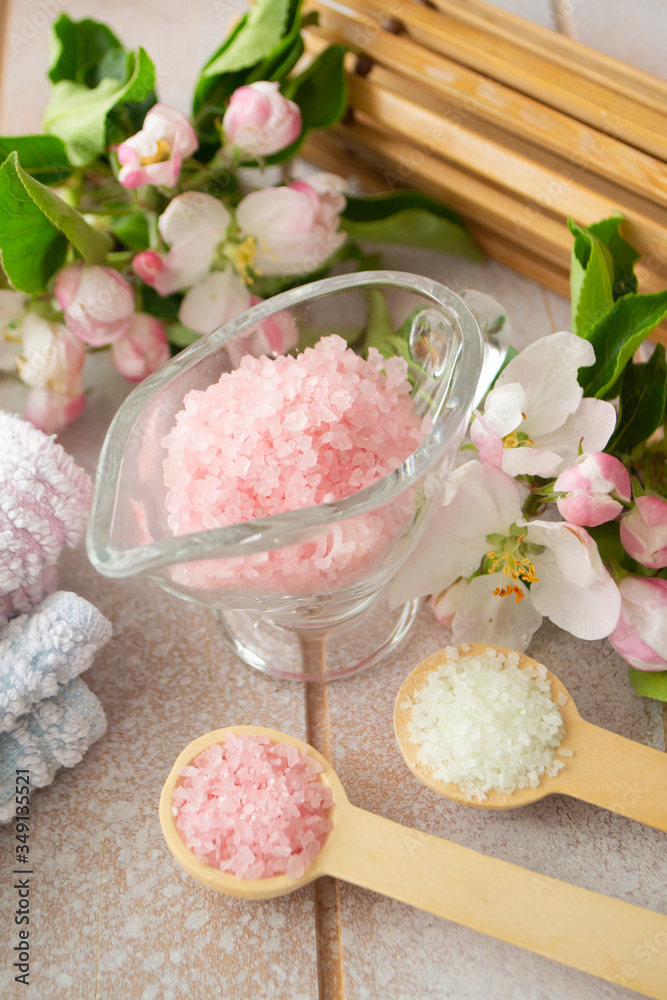 Spa or wellness setting. Pink sea salt, towels and apple blossom on shabby wooden background.
