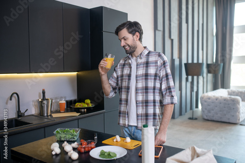 Photos Smiling man with glass of juice standing near the table.