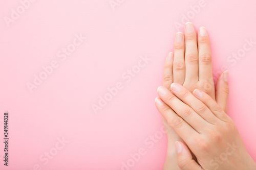 Young woman hands without nail polish on light pink background. Pastel color. Simple manicure. Closeup. Empty place for text. Top down view.