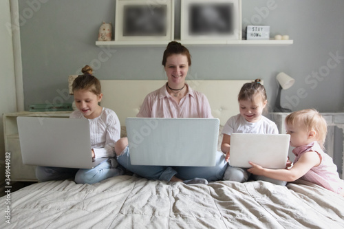 Mom and Three children sitting on bed with laptops