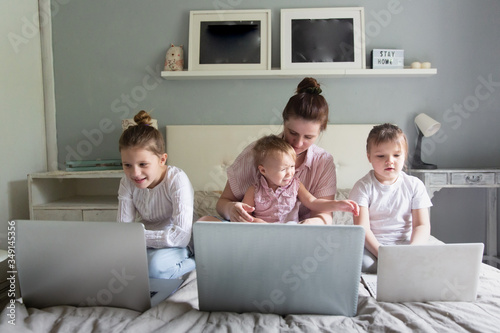 Mom and Three children sitting on bed with laptops