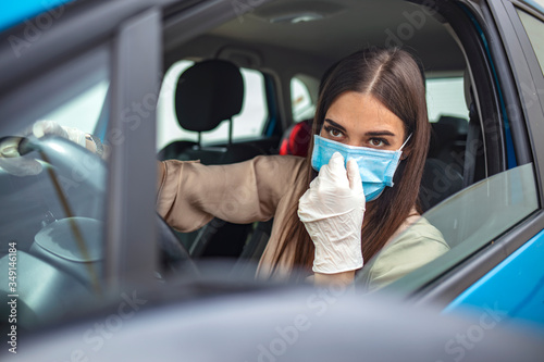  Infection prevention and control of epidemic. World pandemic. Stay safe. Young woman wearing protective face mask while driving car. Protection against the novel coronavirus infection.
