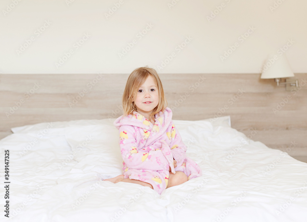 Happy morning! little girl sitting in a bathrobe on the bed Happy morning! little girl sitting in a bathrobe on the bed