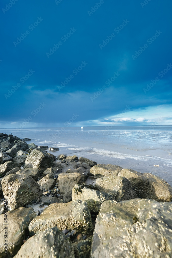 A container ship has lost a cargo at sea, off the coast of Friesland, the Netherlands. A freezer floats at sea, environmental pollution, rocks in foreground. Unesco world heritage