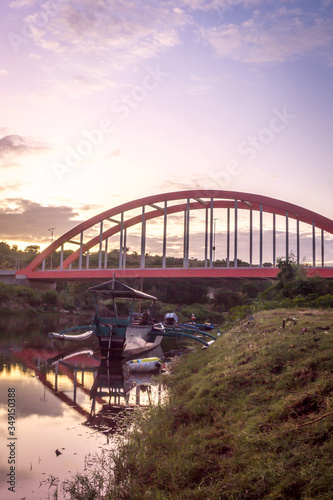 Sunrise at Samota Bridge in Sumbawa City, Indonesia. There is a traditional wooden boat too under the bridge © Harry