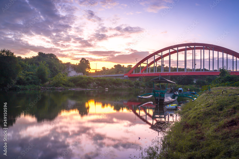 Naklejka premium Sunrise at Samota Bridge in Sumbawa City, Indonesia. There is a traditional wooden boat too under the bridge