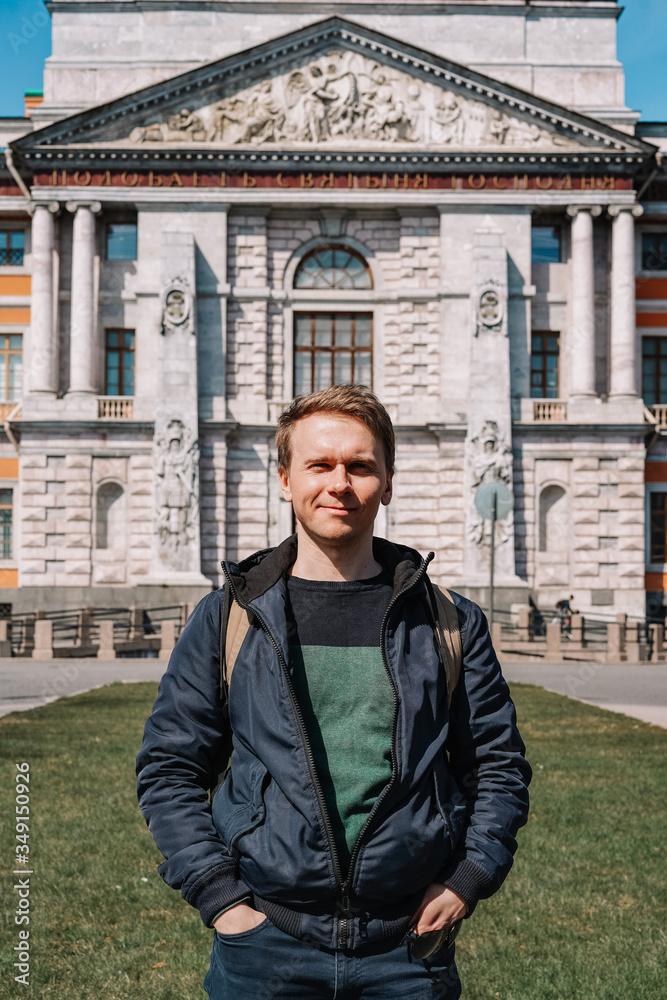 Portrait of a young man in a jacket and with a backpack on the background of an architectural monument, a historical castle in Saint Petersburg