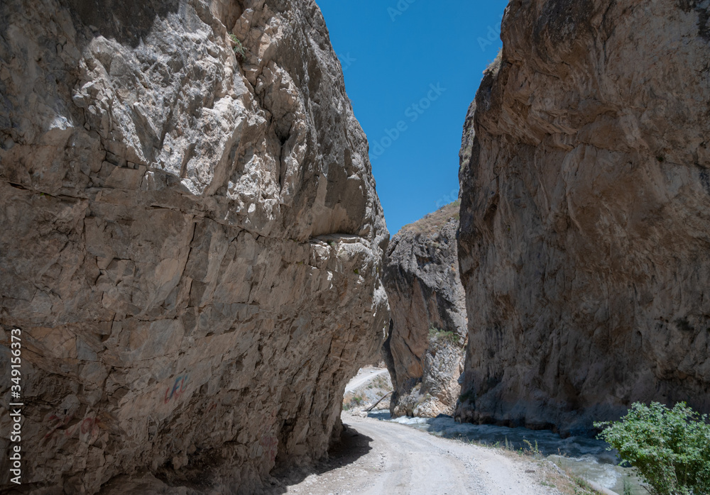 mountains of Central Asia. a narrow road between mountains. rapid river and sparse vegetation. there are no people.
