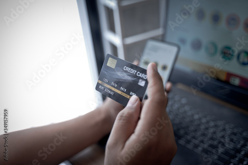 Fototapeta Naklejka Na Ścianę i Meble -  Man holding mock up banking card  while using and typing on laptop. Shopping and payment online.