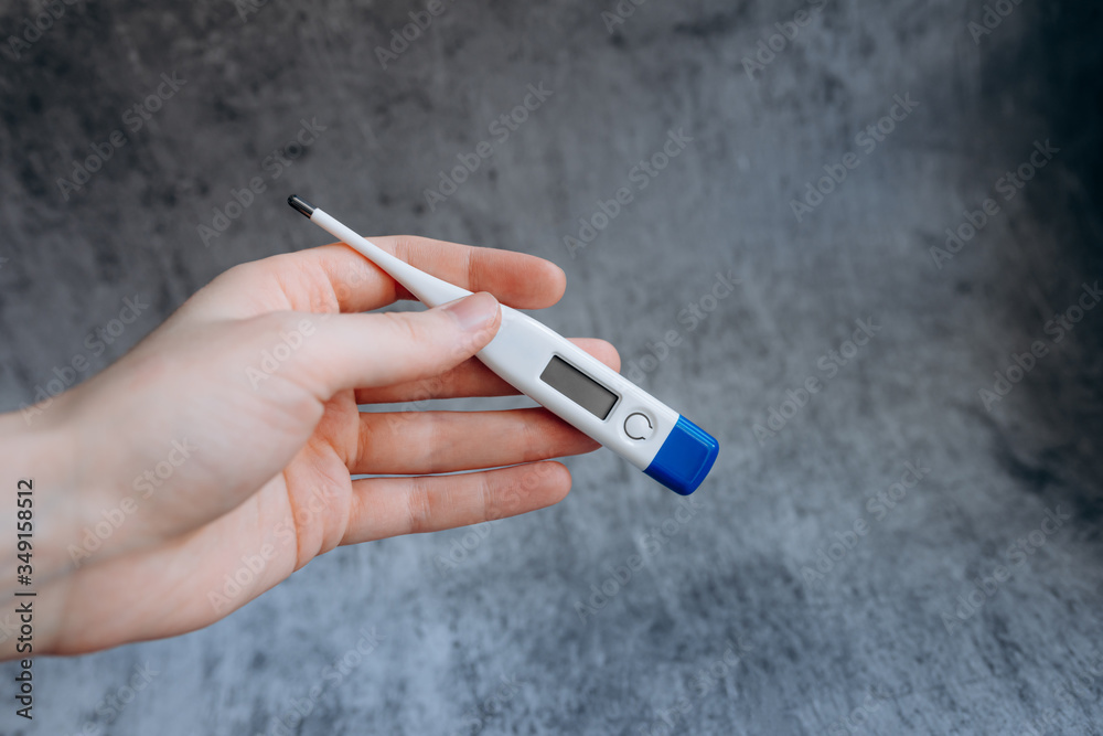 electronic thermometer with normal temperature in woman's hand on a gray texture background