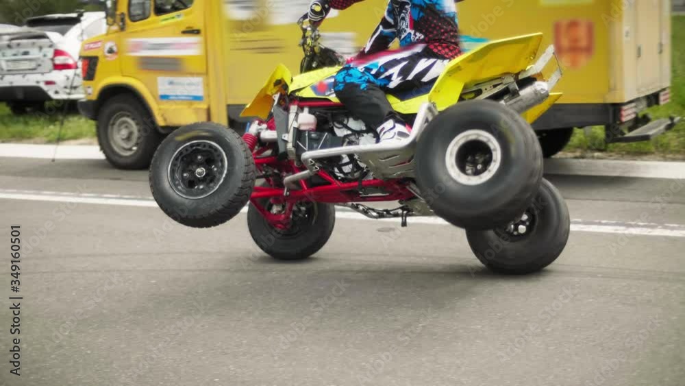 A man performs a stunt and rides an ATV on two wheels on the road.