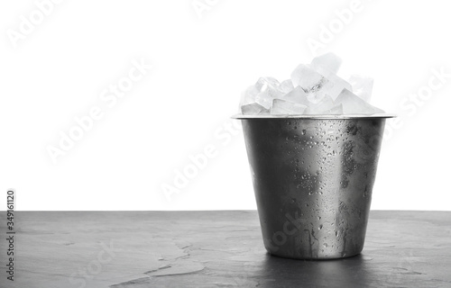 Metal bucket with ice cubes on table against white background