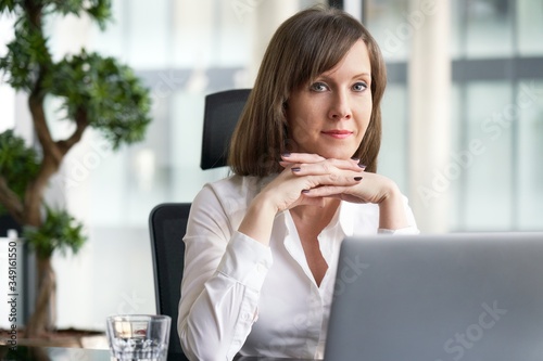 Portrait of white businesswoman in office - sitting at office desk  thinking  working with laptop computer.