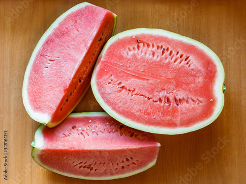 Two quarters and half a sweet ripe watermelon with juicy pink-red pulp lie on a flat surface
