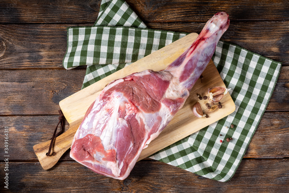Raw lamb leg on a bone on a wooden Board on a brown wooden table. Sheep meat close-up. A fresh piece of lamb meat is on the table. Top view with space for text