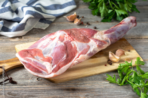 Raw mutton leg on a bone on a wooden Board on a gray wooden table. Sheep meat close-up. A fresh piece of lamb meat is on the table
