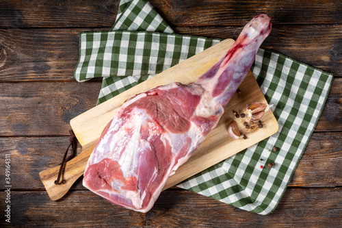 Obraz na płótnie Raw lamb leg on a bone on a wooden Board on a brown wooden table. Sheep meat close-up. A fresh piece of lamb meat is on the table. Top view with space for text w salonie