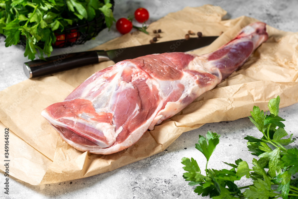 Fototapeta premium Raw mutton leg on the bone on parchment on the gray kitchen table. Sheep meat close-up. A fresh piece of lamb meat is on the table