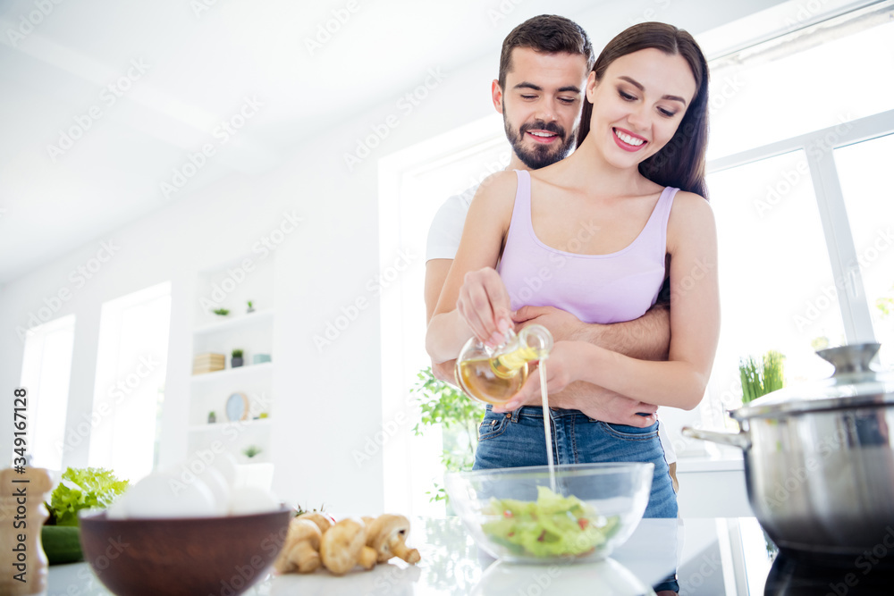 Low angle view photo of two people spouses stay home quarantine prepare dish lunch fresh salad man hug embrace woman pour oil bowl in house kitchen indoors Low angle view photo of two people spouses stay home quarantine prepare dish lunch fresh salad man hug embrace woman pour oil bowl in house kitchen indoors