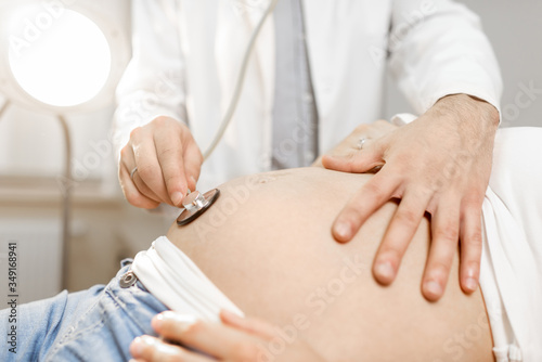 Doctor listening to a pregnant woman s belly with a stethoscope during a medical examination  close-up view