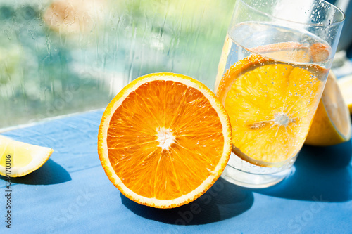 half a juicy ripe orange and a glass of transparent water with gases and bubbles and a round slice of orange inside. Take vitamin C, restore health, lead a healthy lifestyle