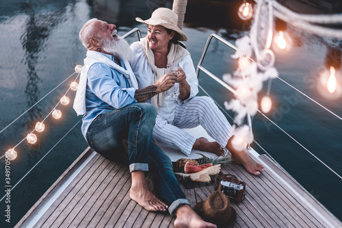 Senior couple cheering with champagne on a sailboat during summer vacation - Old people having fun together drinking and laughing - Joyful elderly lifestyle, travel and love concept