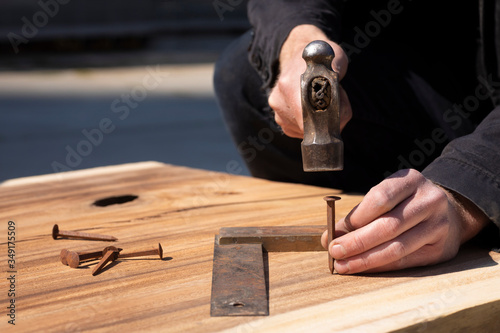 Hands of a carpenter holding a ball peen hammer to driving a rusty old nail into a piece of wood. Measuring tool on the background. Diy, authentic making