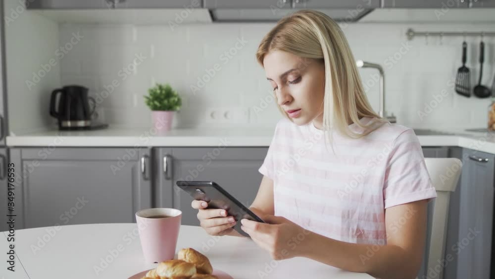 Sad woman using tablet device while having breakfast on her kitchen Sad woman using tablet device while having breakfast on her kitchen