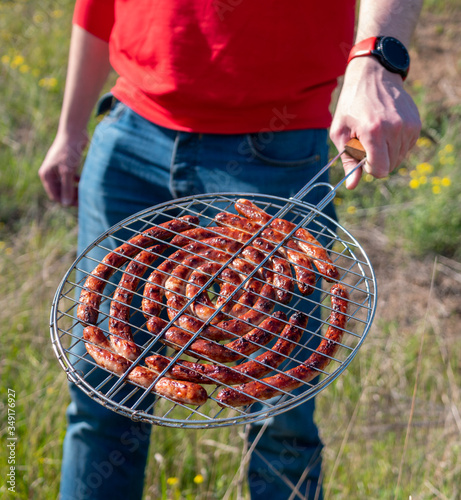 Man holding grilling basket with Bavarian sausages. Grilling sausages on barbecue grill. BBQ outside.