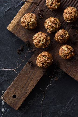 Healthy food concept. Homemade oatmeal bites and dry alder tree branch with cones on oak board on black background top view