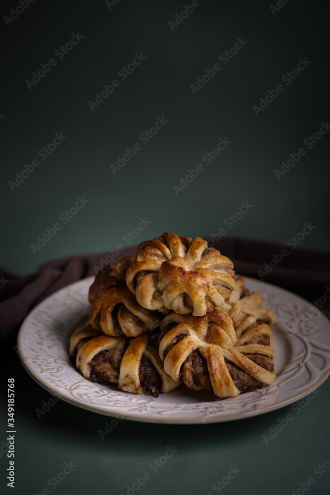 Fresh pastries, hot tasty cinnamon rolls on a green background with a burgundy dishcloth. Buns for dessert for hot drinks. Top view. Fresh pastries, hot tasty cinnamon rolls on a green background with a burgundy dishcloth. Buns for dessert for hot drinks. Top view.