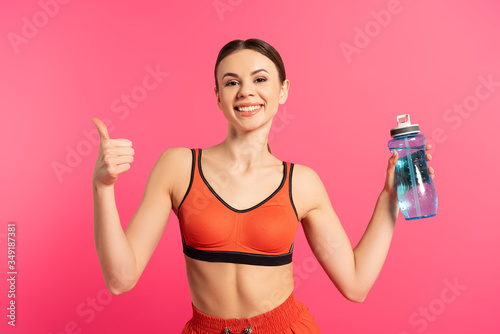happy sportswoman showing thumb up and holding sports bottle with water isolated on pink © LIGHTFIELD STUDIOS