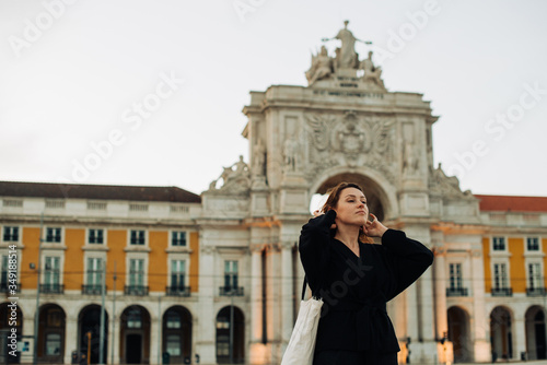 Half length portrait of millennial caucasian woman wearing black  standing alone in the evening at Praca do Comercio  Commerce Square  under Triumphal arch  famous tourist attraction in Lisbon