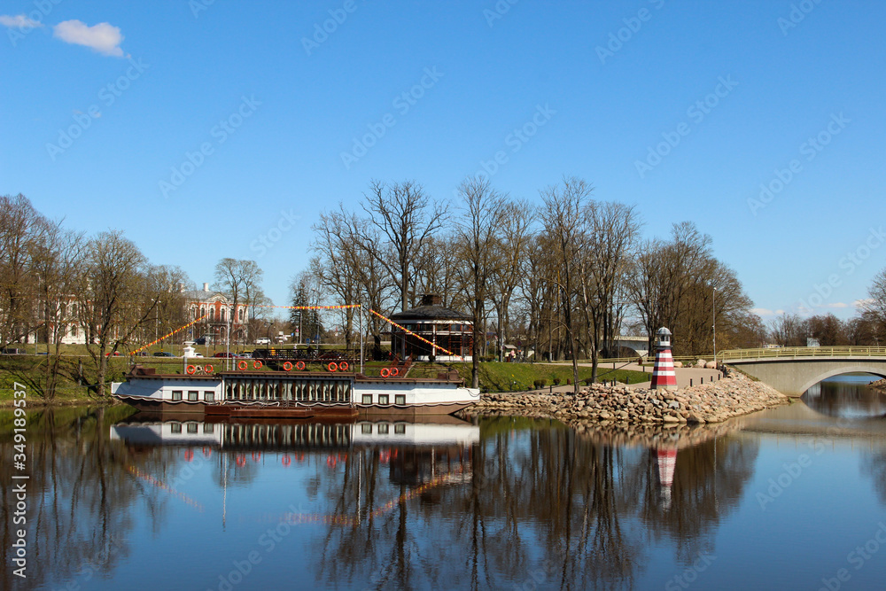 City canal with decorative lighthouse and steam-ship at the coast. Popular waterscape in the city of Jelgava.