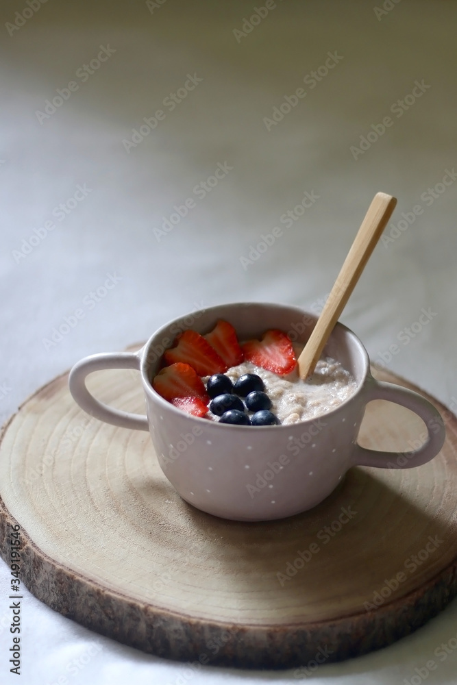 Bowl of vegan porridge with strawberry and blueberry topping, served in bed. Selective focus. Bowl of vegan porridge with strawberry and blueberry topping, served in bed. Selective focus.