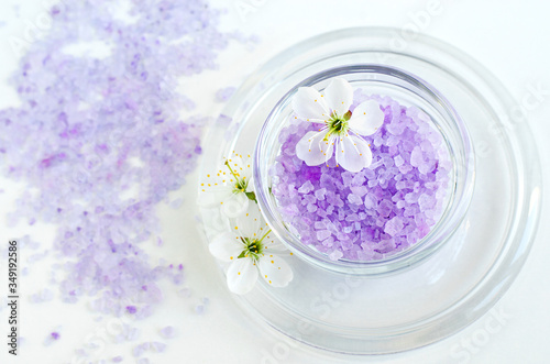 Small glass bowl with purple bath salt (foot soak) and white flowers. Top view, copy space.
