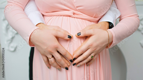 Pregnant Belly with fingers Heart symbol. Beautiful Young Pregnant Woman and Her Husband Together Caressing Her Pregnant Belly. Pregnancy. Love Concept. Mom and Dad waiting for newborn baby. Parents