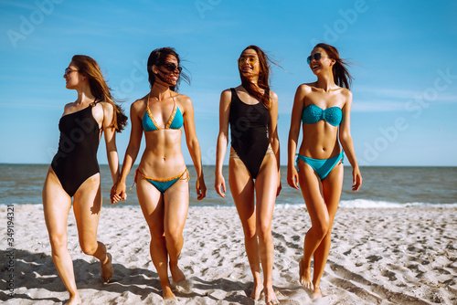 Portrait of young female friends walking on the sea shore looking at camera laughing. Happy  four girls strolling along a beach. Summer, relax and lifestyle concept.