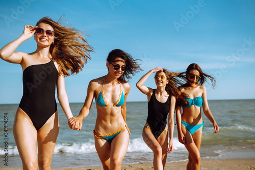 Portrait of young female friends walking on the sea shore looking at camera laughing. Happy  four girls strolling along a beach. Summer, relax and lifestyle concept.