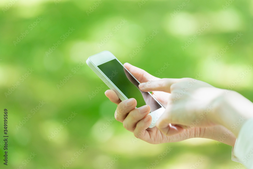 新緑の中でスマートフォンを使う若い女性の手元 新緑の中でスマートフォンを使う若い女性の手元
