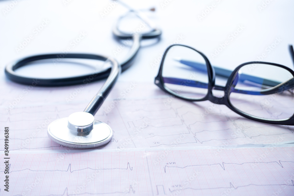 cardiogram with stethoscope, pen, magnifier, pills and glasses lay on a table