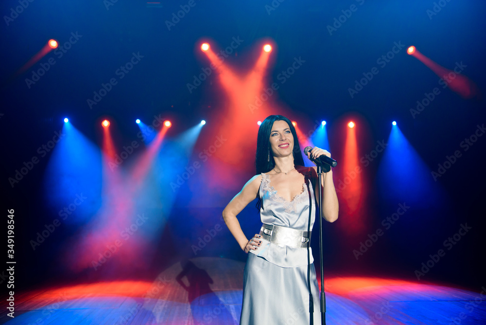 A female singer holding microphone against the colorful lights of the scene. Bright background with neon lights.