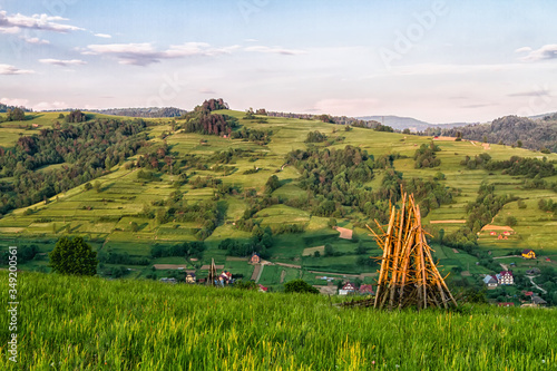 Fototapeta Naklejka Na Ścianę i Meble -  Traditional Slovenian constructions for drying hay and wood storage, hayrack on the hilly field in Beskid Sadecki mountains, Poland. Lomnica Zdroj and Piwniczna towns in the background.