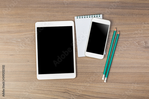 White digital tablet and mobile phone on an office working dark wooden table.