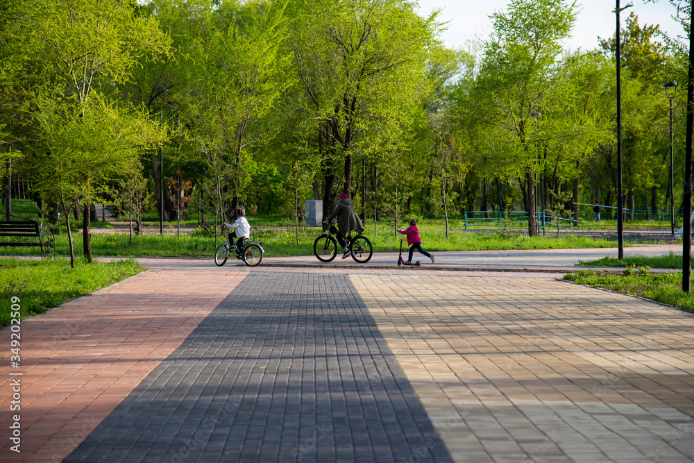Children and adult ride bicycles and a scooter in the park. Children and adult ride bicycles and a scooter in the park.